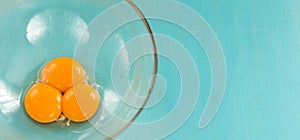 Three fresh raw egg yolks in a glass bowl prepared for whipping on a blue background. Top view