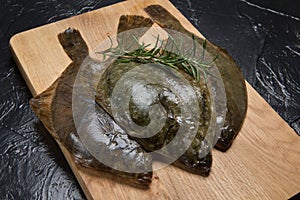 Three fresh raw flounders and sprigs of rosemary on a cutting board, sea fish