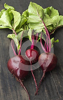 Three fresh red beets with leaves on a wooden background