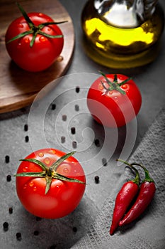 Three fresh red ripe tomatoes with drops for use as cooking ingredients, olive oil bottle, black and chili pepper