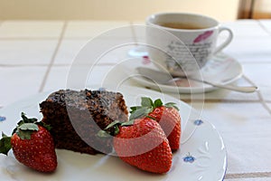 Three fresh red strawberries around a delicious and tasty chocolate cake and a cup of coffee at background