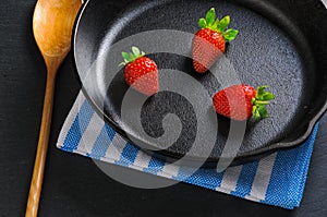 Three fresh red strawberries on black cast-iron pan served with wooden spoon and napkin. Concept