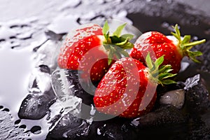 Three fresh red strawberries on slate stone with ice