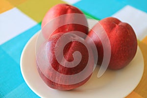 Three Fresh Ripe Nectarine Whole Fruits on White Plate Served on Vibrant Color Tablecloth