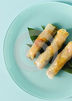 Three fresh spring rolls stuffed with seafood and vegetables on a light gray flat plate .