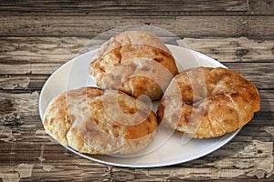 Three Freshly Baked Pitta Bread Loaves On White Porcelain Plate Set On Old Wooden Cracked Flaky Picnic Table