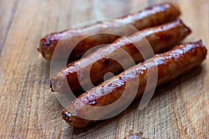 Three freshly fried sausages lie diagonally on a wooden board