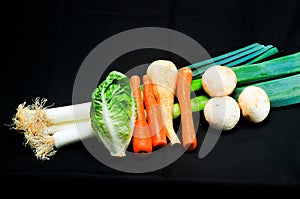 three freshly pulled leeks, carrots and mushroom, with a turnup half and small head of lettuce, on black background