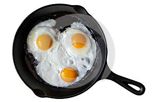 Three fried eggs in cast iron frying pan isolated on white from