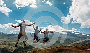 Three Friend Jumping Holding Hands Mountains Elbrus Landscape On Background. Lifestyle Travel Happy Emotions Success Concept Summe