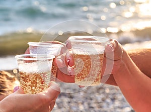 Three friends at the beach are drinking sparkling wine at sunset