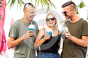 three friends cheerful company rest on a tropical beach and drink cocktails, very, magazine concept