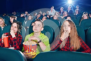 Three friends eating popcorn by watching movie.