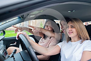 Three friends go on a trip. Caucasian women drive in a car and point fingers in surprise.