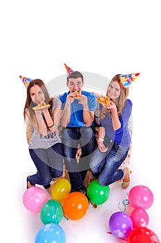 Three friends with hats and balloons eating pizza