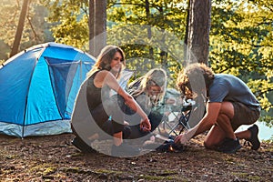 Three friends hiking in the forest and try to light a fire at camp.