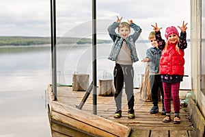 Three friends play fishing on wooden pier near pond. Two toddler boys and one girl at river bank. Children having fun doing grima