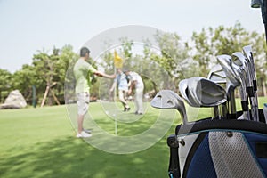 Three friends playing golf on the golf course, focus on the the caddy