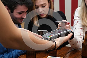 Three friends seeing something on their smartphone, and paying with credit card.
