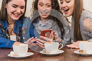 Three friends sitting in a cafe with a smart phone and having a funny conversation. Good girls with long beautiful black