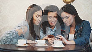 Three friends sitting in a cafe with a smart phone and having a funny conversation. Good girls with long beautiful black