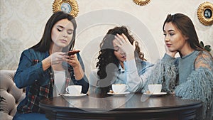 Three friends sitting in a cafe with a smart phone and having a funny conversation. Good girls with long beautiful black