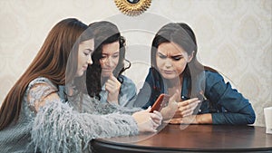 Three friends, sitting in a coffee shop using a smart phone and having a funny conversation. Good girls with long