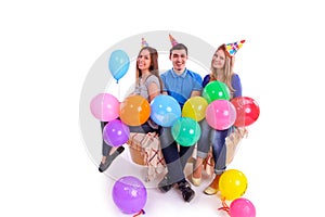 Three friends sitting on a couch with balloons and hats