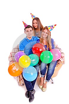 Three friends sitting on a couch with hats and balloons