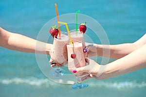 Three fruit juice smoothie in classic glass cups of berry fruits turquois sea water background. Three girls cheers