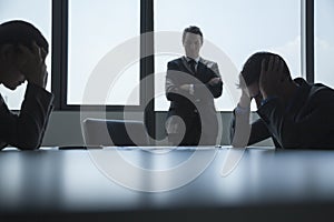 Three frustrated and overworked business people in the board room with arms crossed and head in hands.