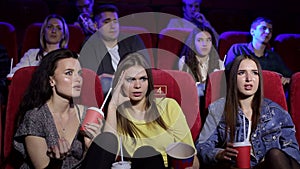 Three frustrated young girls watching an uninteresting movie at the cinema.