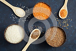 Three full bowls of cereals lentils, rice and buckwheat on a dark blue background.