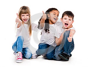 Three funny children sitting on the floor with thumbs up