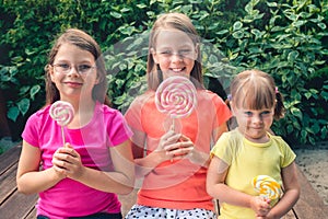 Three funny little girls in colorful T-shirts with large lollipops
