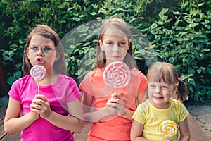 Three funny little girls in colorful T-shirts with large lollipops