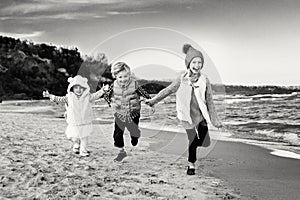 Three funny smiling laughing Caucasian children kids friends playing running on ocean sea beach