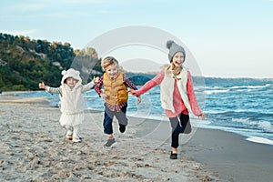 Three funny smiling laughing white Caucasian children kids friends playing running on ocean sea beach on sunset outdoors