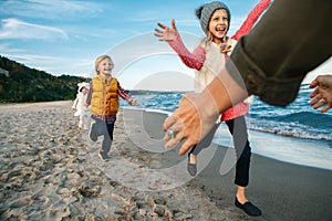 Three funny smiling laughing white Caucasian children kids friends playing running to mother parent adult on ocean sea beach