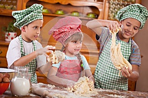 Three funny young child play with a dough in the kitchen