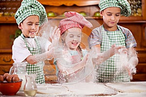 Three funny young child shaking hands with flour in the kitchen