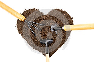 Three garden hand tools in a heart shaped pile of soil