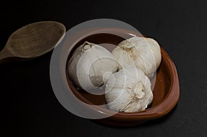 Three garlic in clay pot with wooden spoon