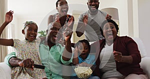 Three generation african american family cheering together while together while watching tv at home