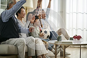 Three generation asian family watching soccer game telecast on tv together at home