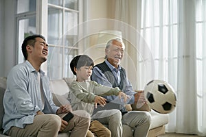 Three generation asian family watching soccer game telecast on TV