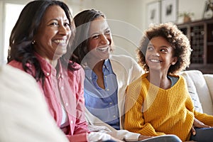 Three generation family female family group sitting on a sofa in the living room watching TV and laughing, selective focus