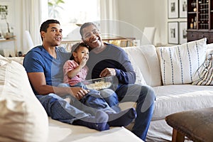 Three generation family male family group sitting on a sofa in the living room eating popcorn and watching TV, selective focus