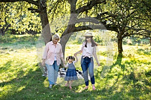 Three generation family, pleasan senior lady, young mom and little cute three years old girl, walking outside in the