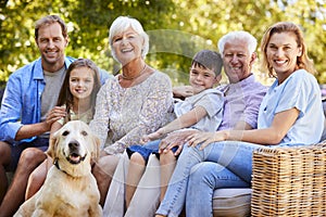 Three generation family sitting with pet dog in the garden